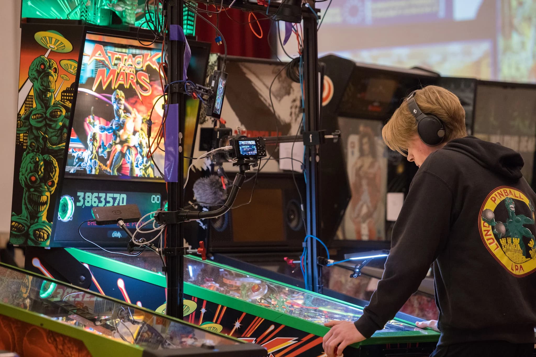 Viggo Löwgren in headphones playing Attack from Mars, seen from behind past the stream camera rig