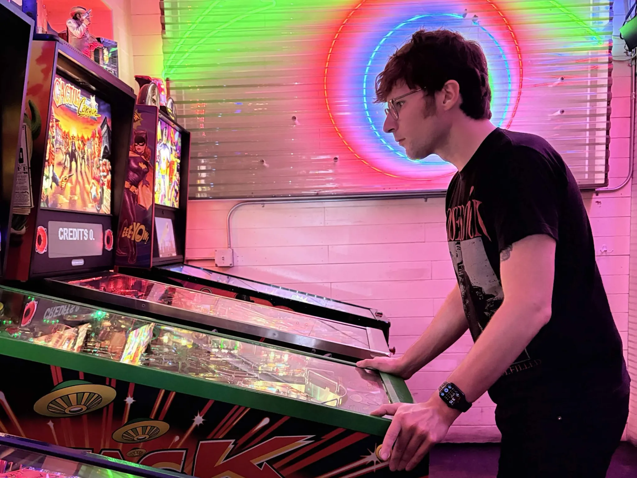 Conor Wilson playing a pinball machine in an arcade lit by neon