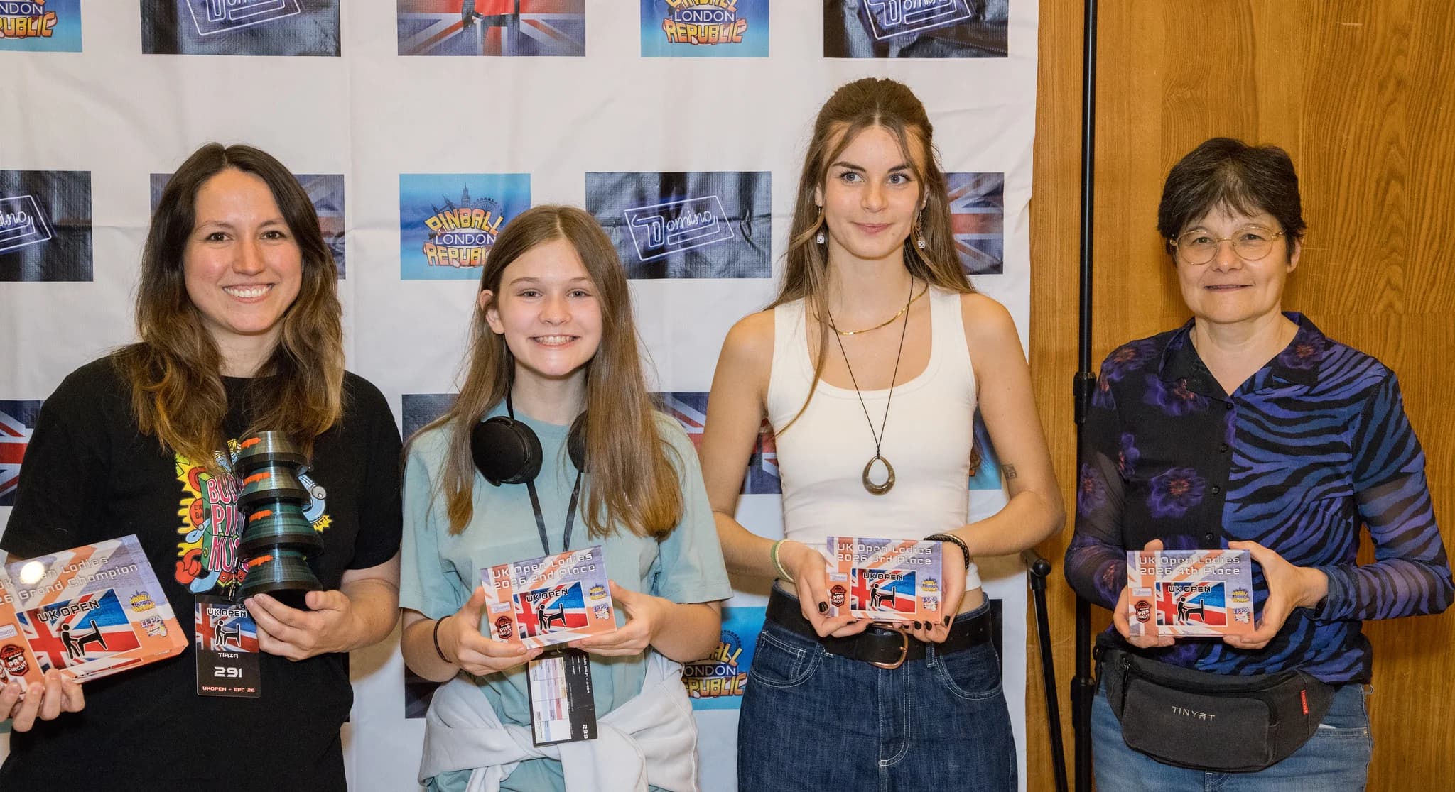 The four UK Pinball Open 2026 Women's finalists holding their awards in front of the event backdrop