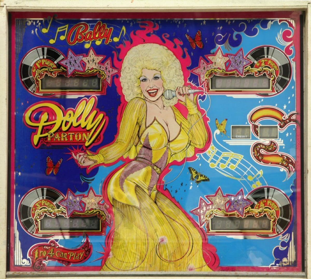 The production Dolly Parton backglass: Parton in a flowing yellow gown holding a microphone against a blue star-filled sky, with butterflies, musical notes and four score displays framed by records and glitter stars