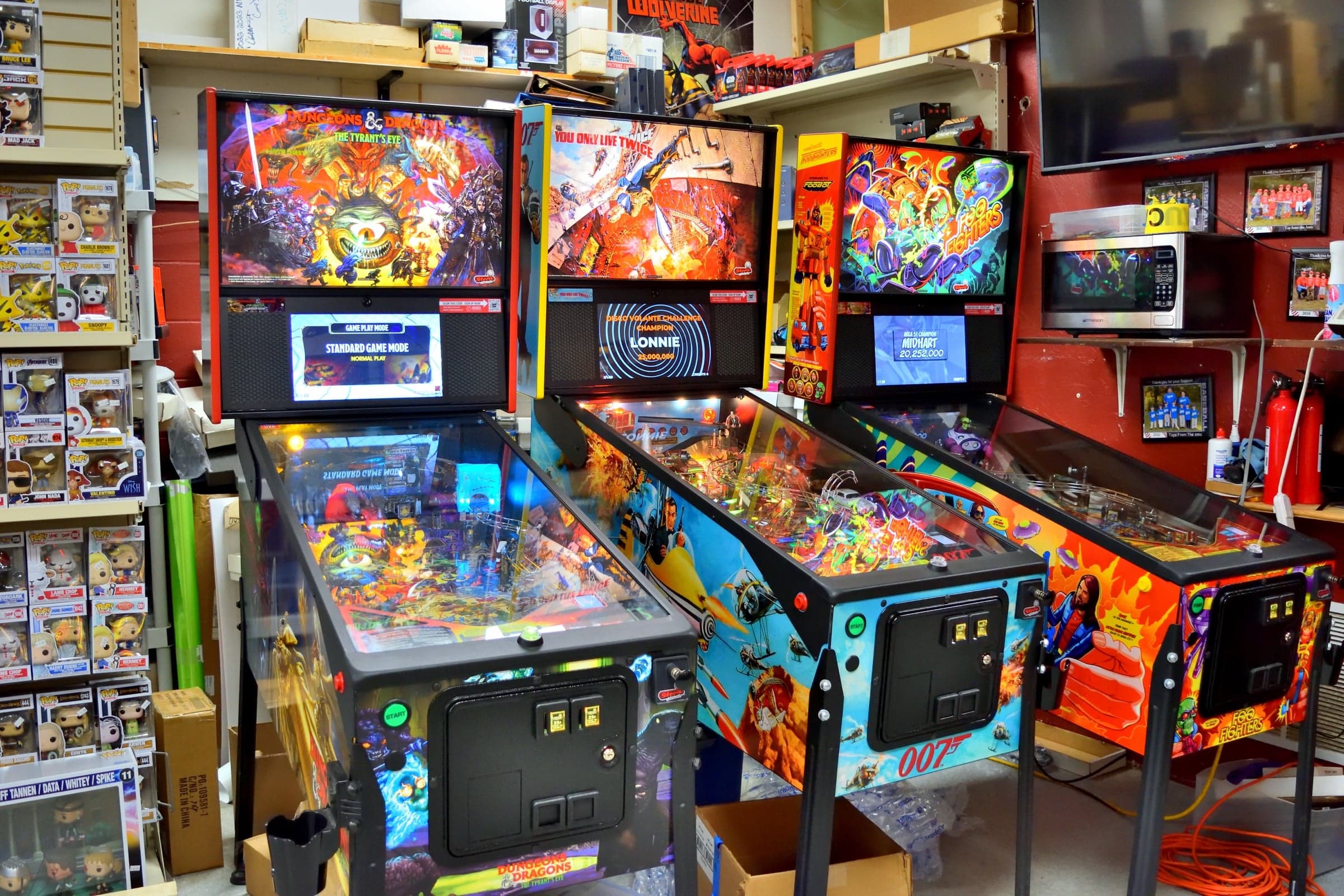 Dungeons and Dragons, James Bond 007 and Foo Fighters pinball machines beside shelves of Funko Pop boxes