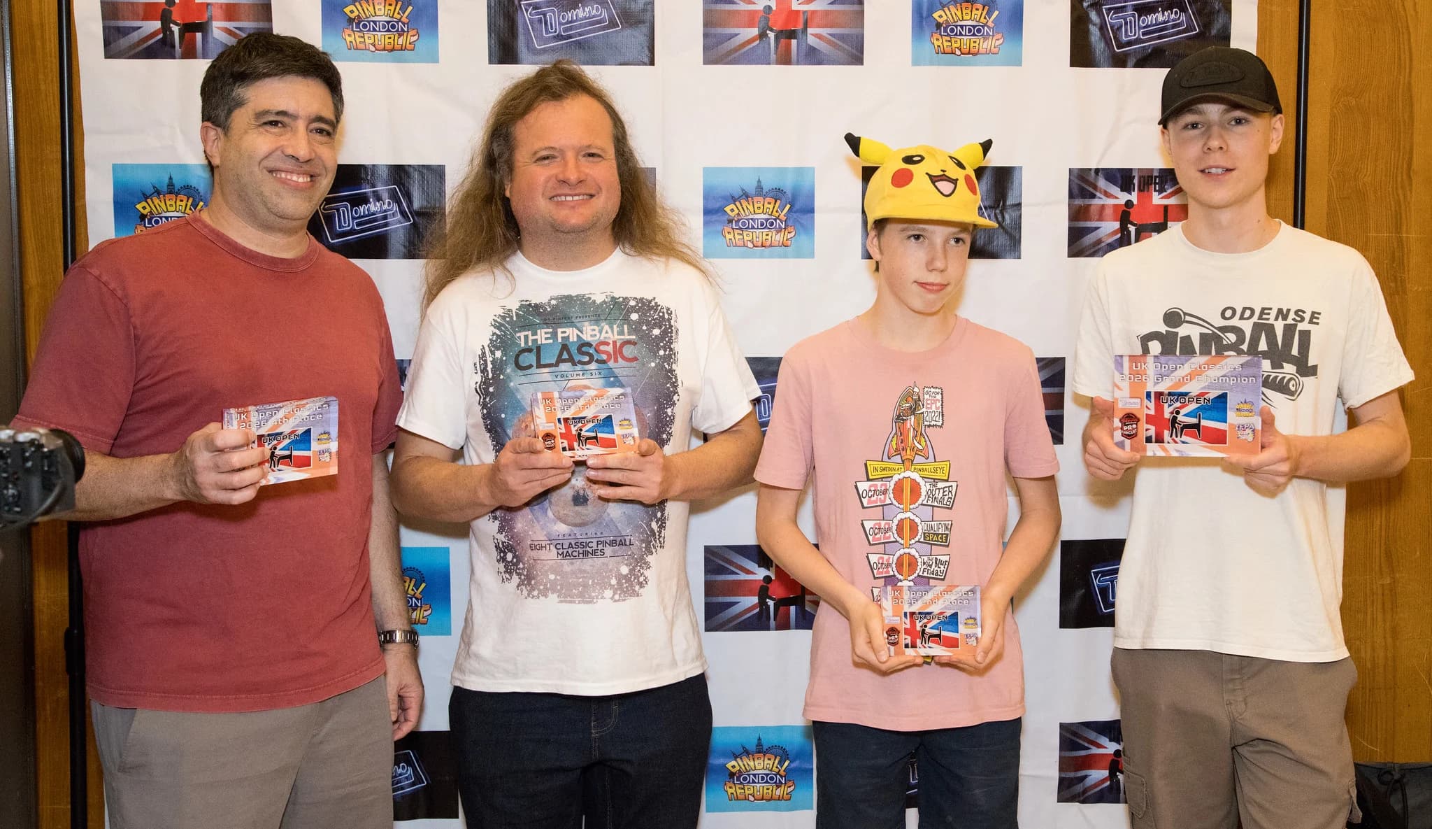 The four UK Pinball Open 2026 Classics finalists holding their awards in front of the event backdrop