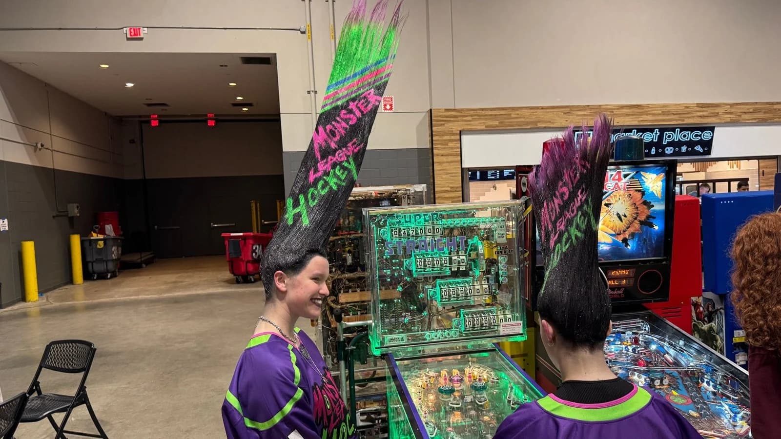 Two cosplayers in Monster League Hockey costumes beside the game