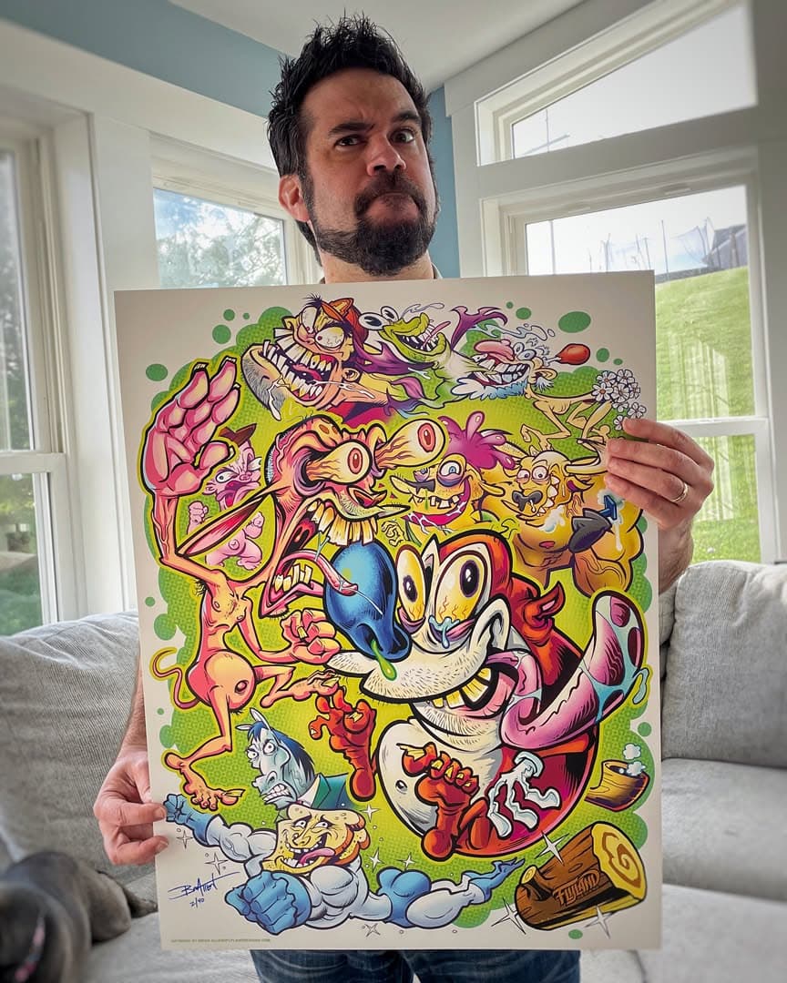 Brian Allen holding up his Ren and Stimpy print, a crowded poster of Ren, Stimpy and characters from the show drawn in his style on a green background