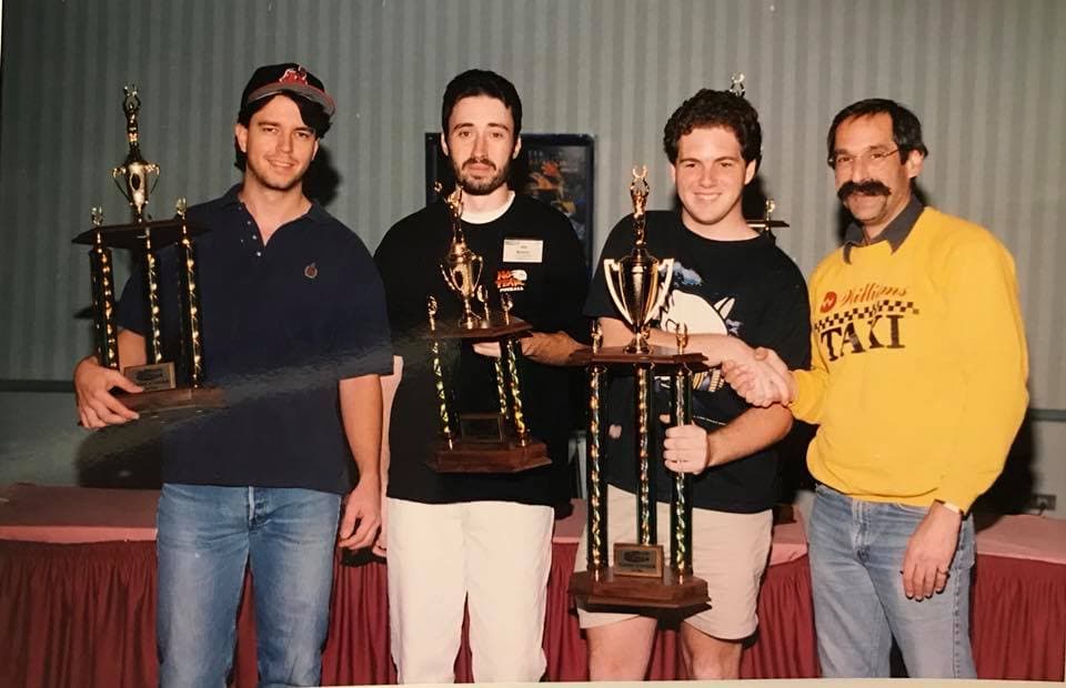 Four men posing with multiple trophies at an awards ceremony