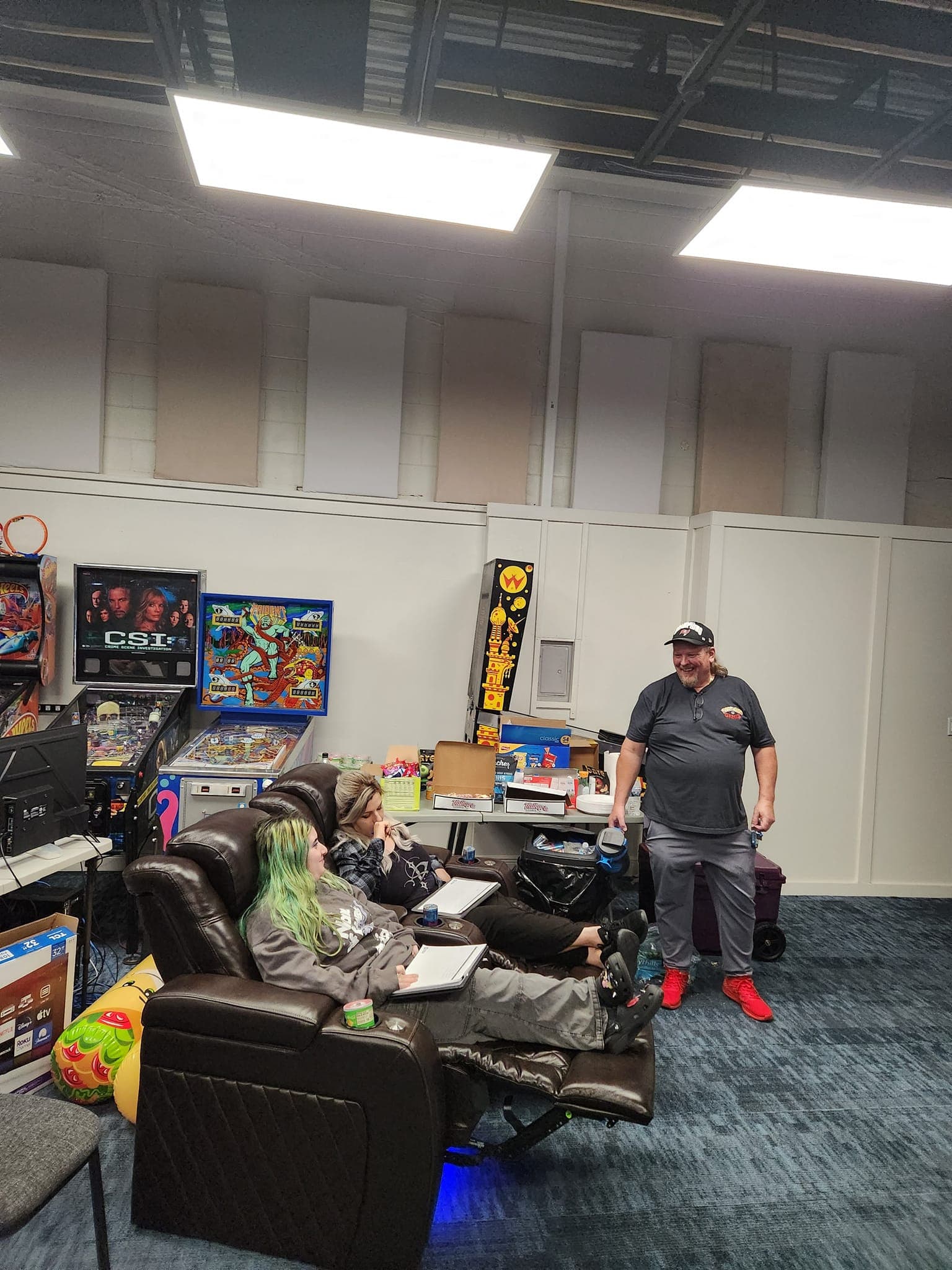 Pinball machines and people in a game room with colorful decor