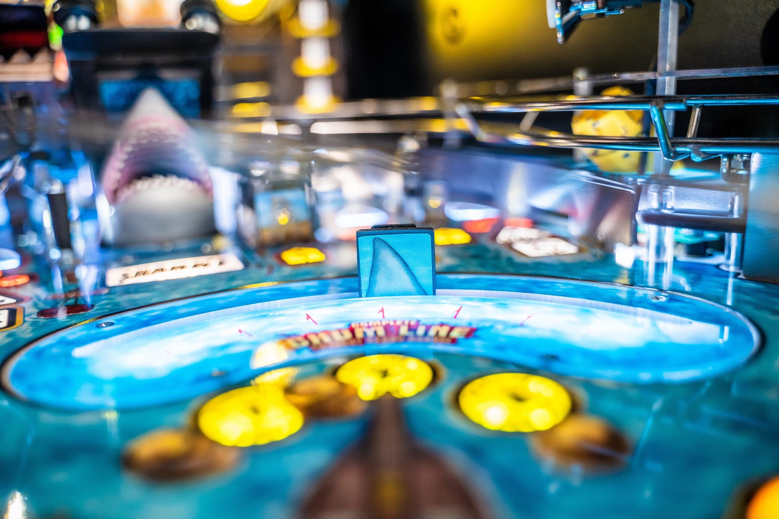 Closeup of a shark-themed pinball machine with blue and yellow details