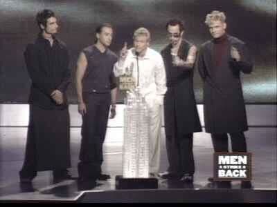 Five men in black and white outfits on stage at Men Back event