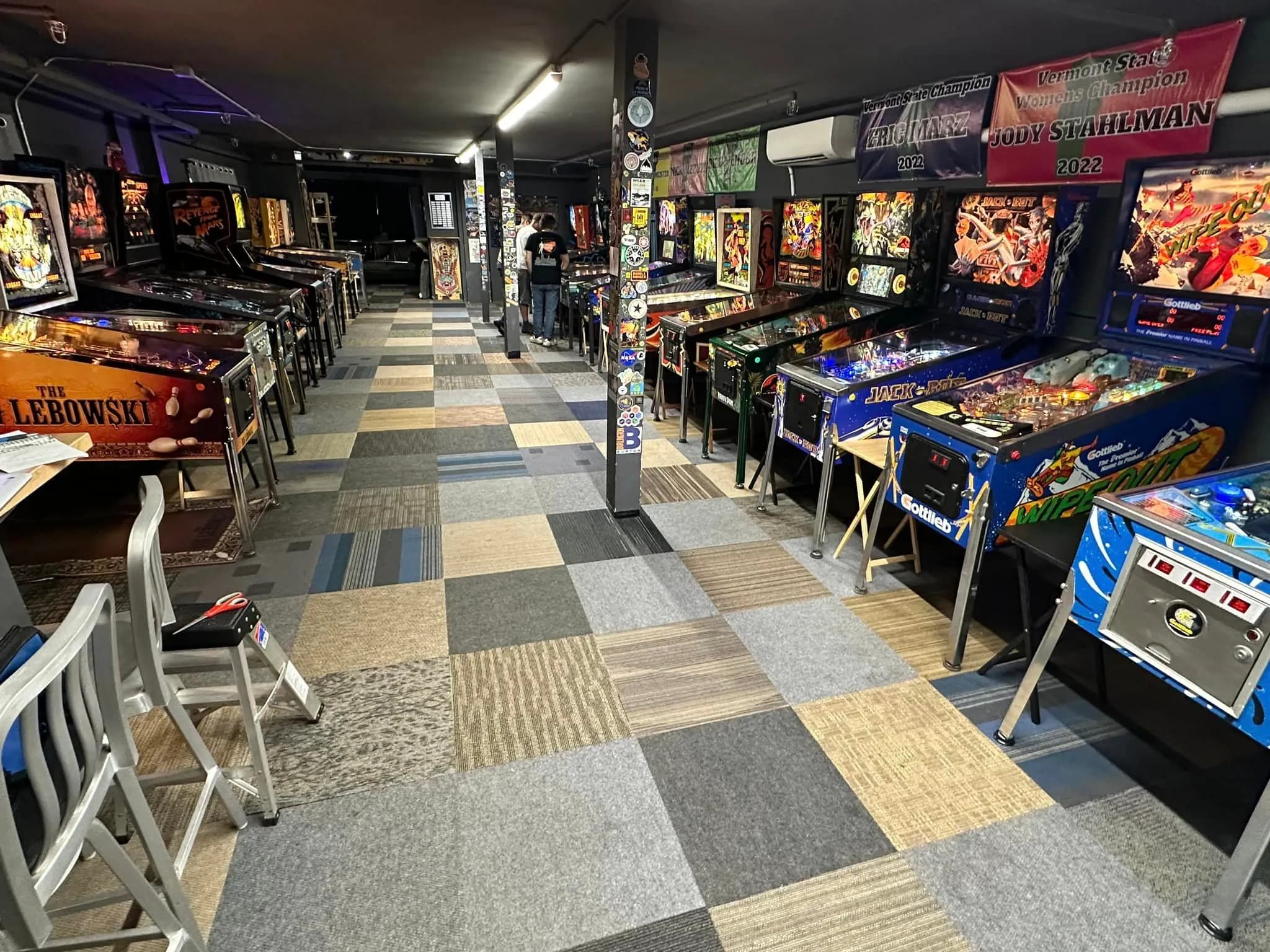 Colorful pinball machines lined up in a game room with checkerboard floor