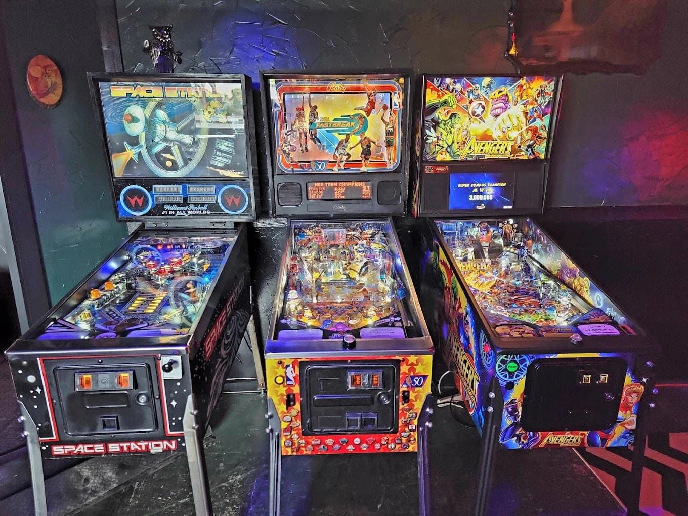 Three vintage pinball machines with colorful themed backboards and playfields