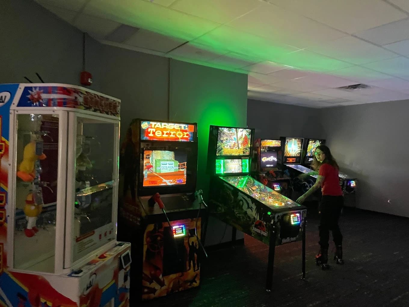 Arcade room with pinball machines and colorful game cabinets under green lighting