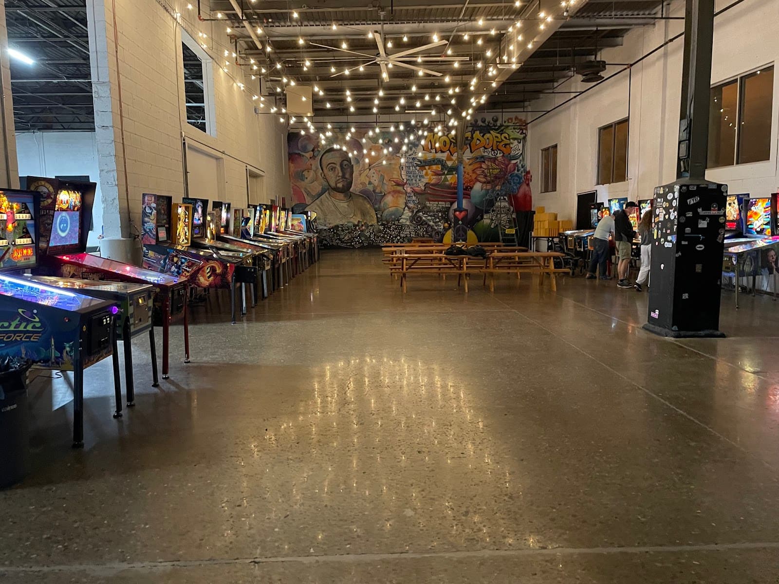 Pinball arcade with string lights, colorful mural, and rows of arcade machines