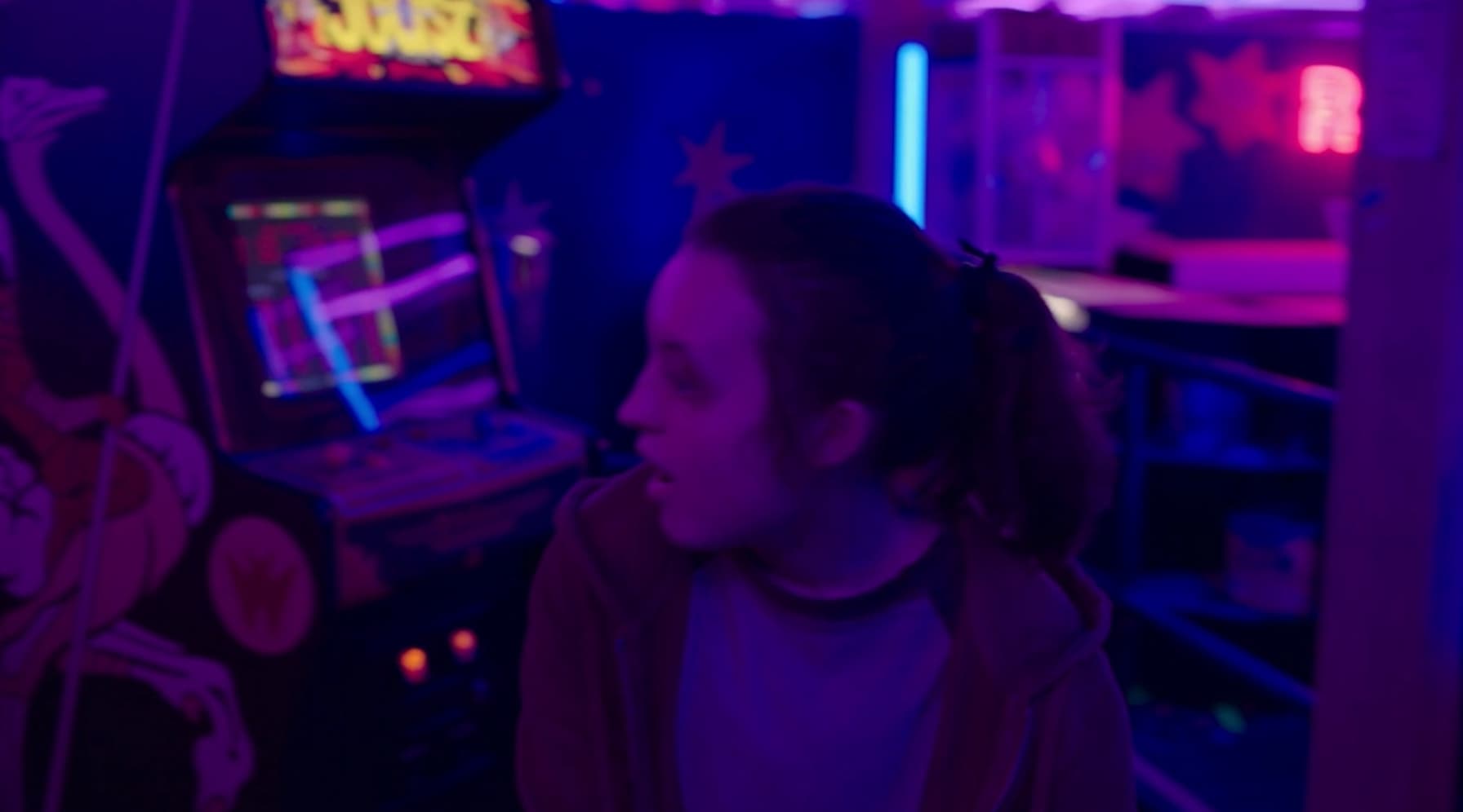 Person in neon-lit arcade, standing near vintage video game machine