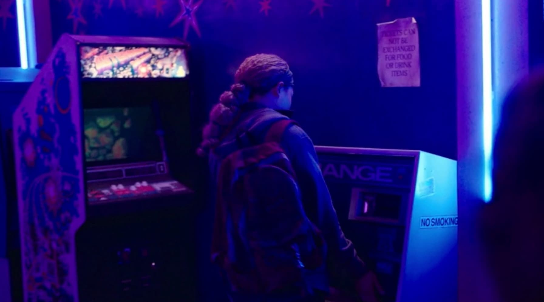Person playing arcade game in neon-lit room with blue and purple lighting