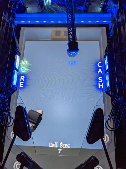 Overhead view of a pinball machine with blue lighting and game screen