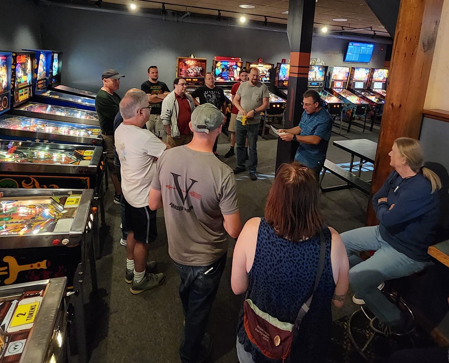 Group of people gathered around pinball machines in a dimly lit arcade