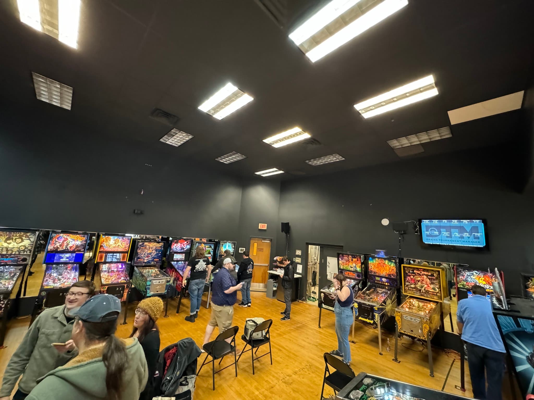 Pinball arcade with multiple machines and players in a dimly lit room