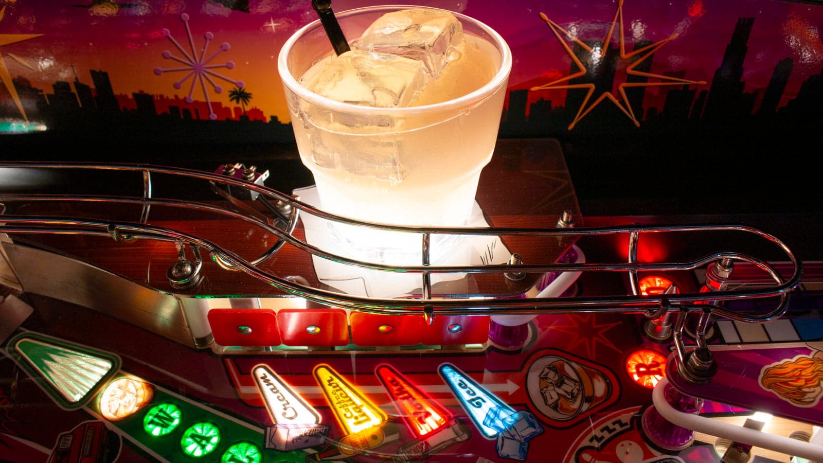 A moulded White Russian sculpt, with ice and a straw, resting on the playfield glass above lit inserts