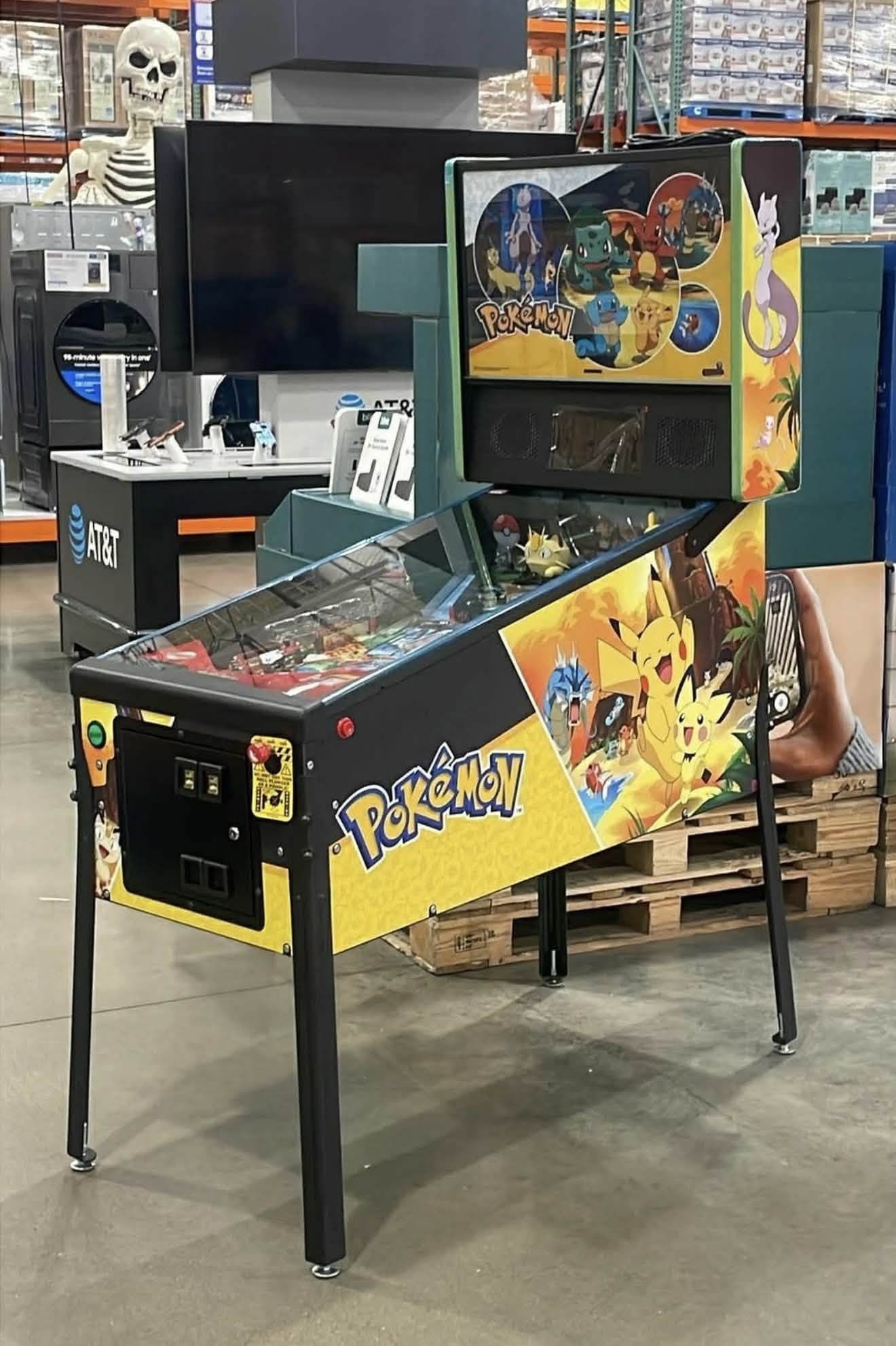 A Stern Pokemon Home Edition pinball machine set up on a Costco sales floor, showing the yellow cabinet art with Pikachu and the Pokemon logo, and the backbox artwork featuring Mewtwo, Bulbasaur, Charmander and Squirtle