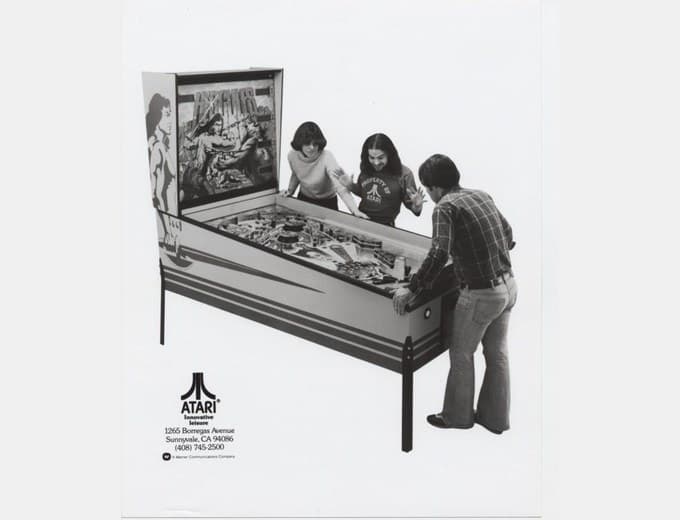 Three people playing the oversized Hercules pinball machine, a black-and-white press photograph, Atari Incorporated, 1979
