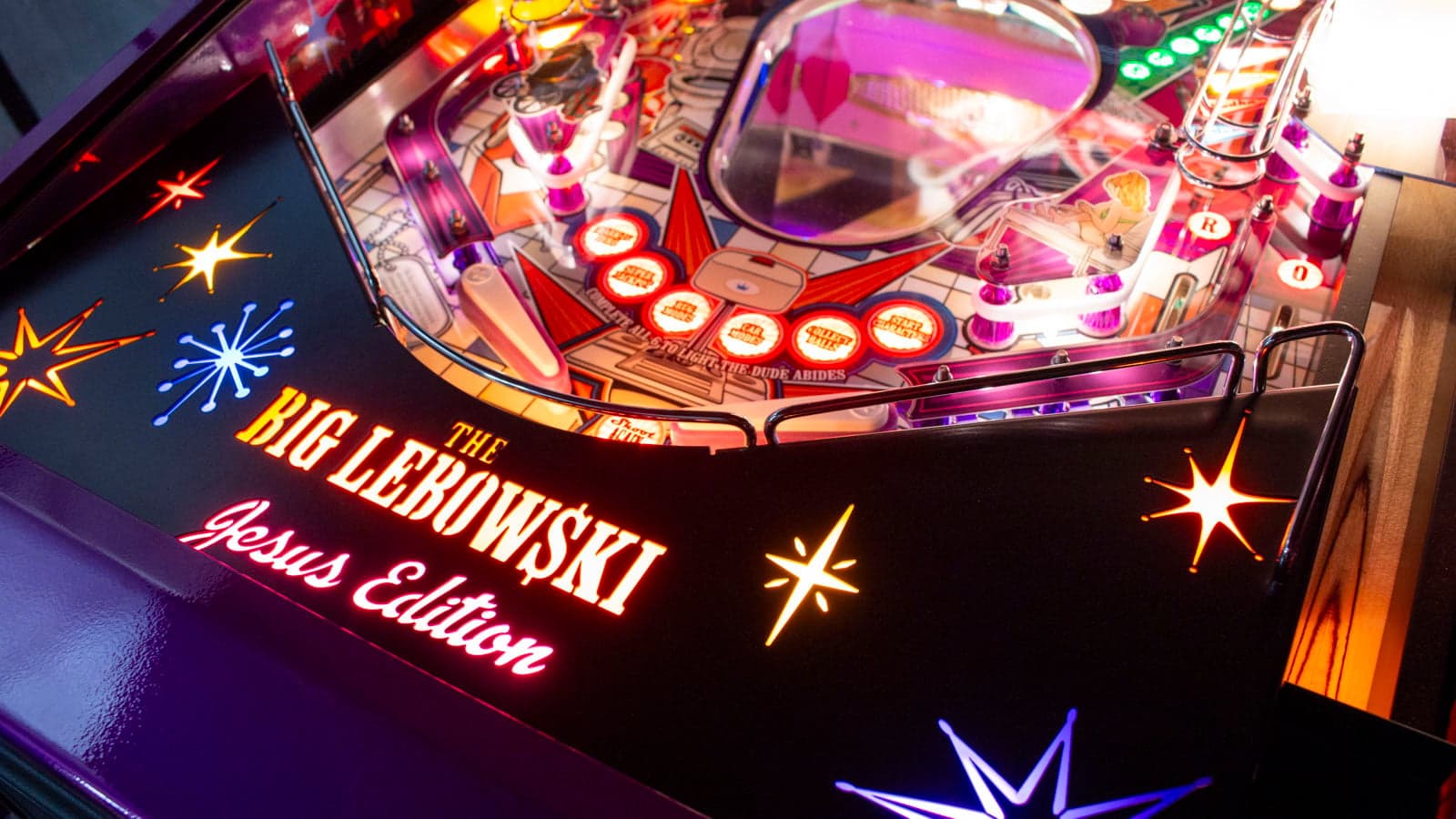 The lower playfield apron, lit, carrying The Big Lebowski Jesus Edition in illuminated type surrounded by lit starbursts