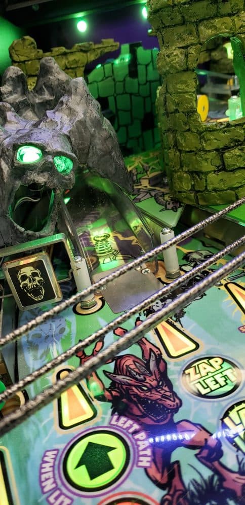 Spooky pinball machine with green lighting, skull, and fantasy creatures