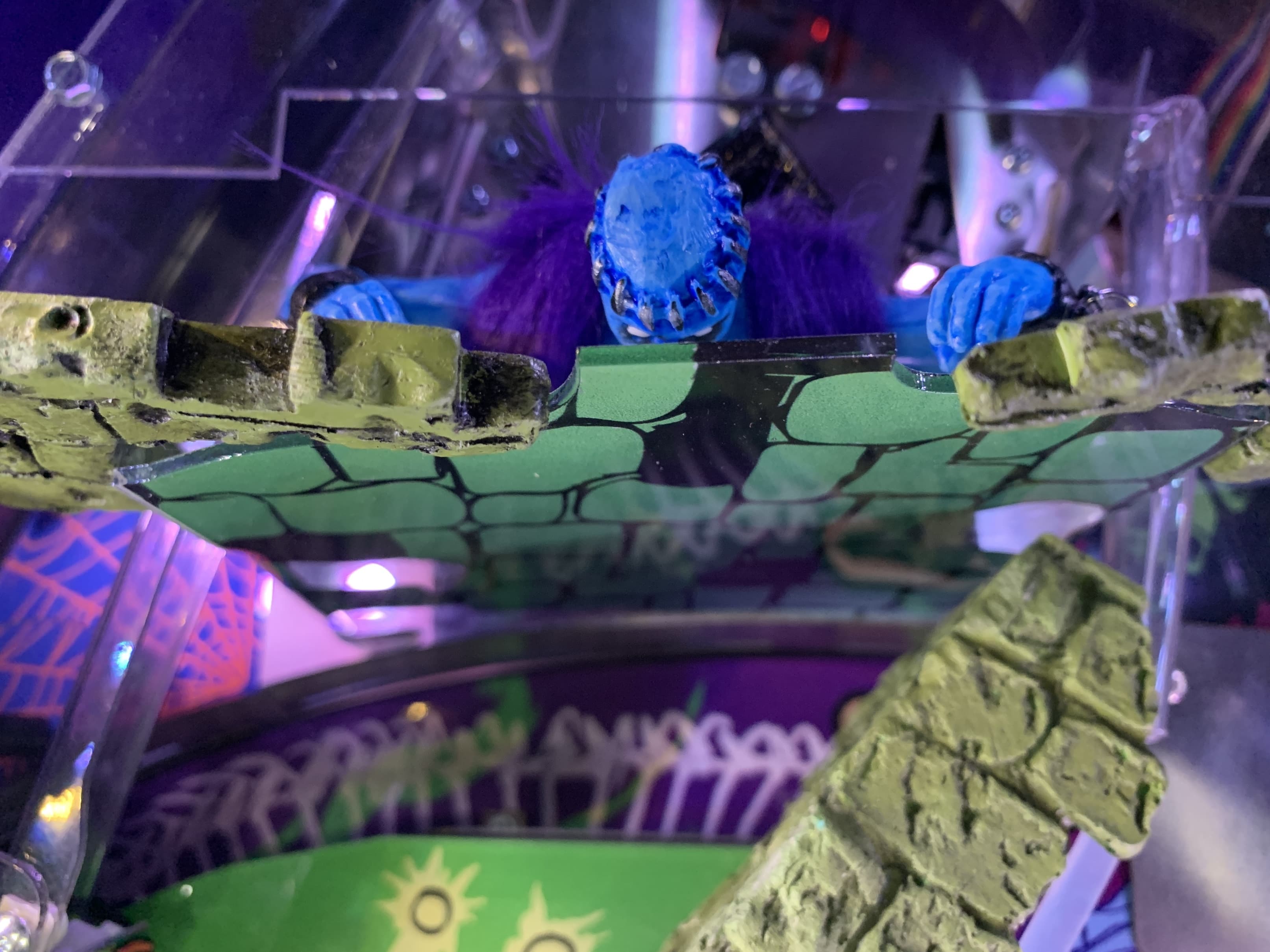 Blue creature with purple hair peers over rocky green platform in sci-fi scene
