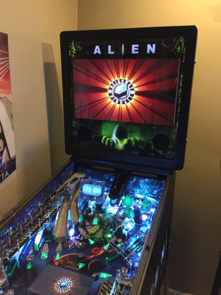Alien-themed pinball machine with colorful illuminated playfield and screen