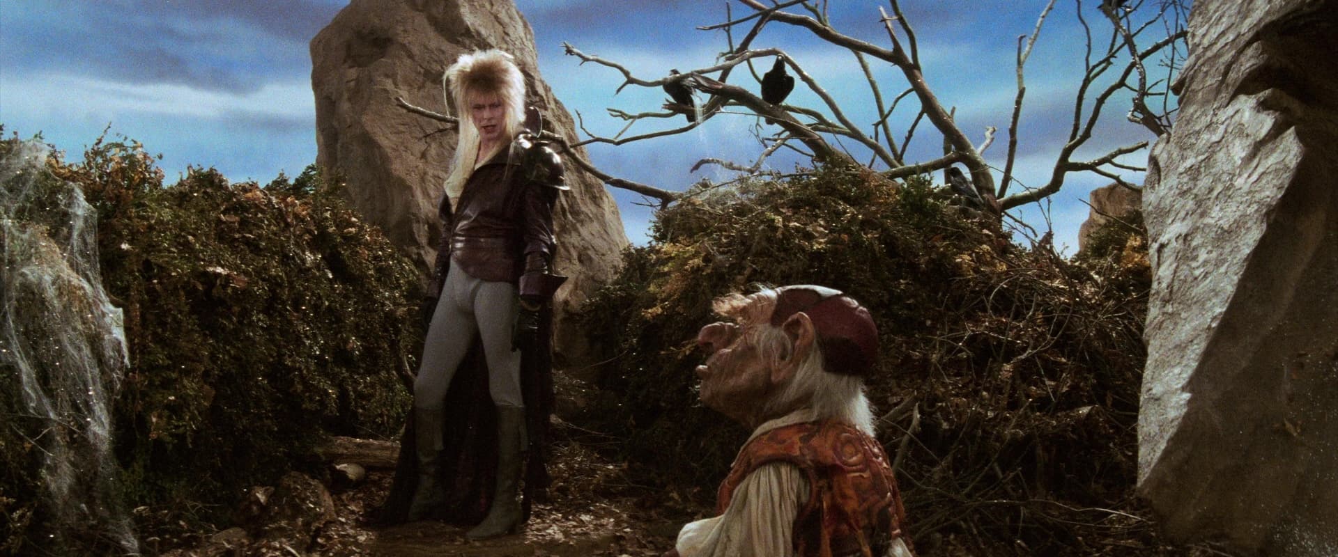 Goblin King confronts magical creature in rocky, desolate fantasy landscape