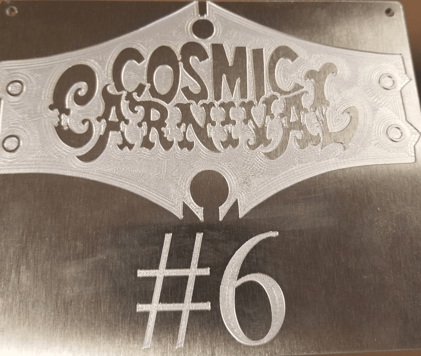 Engraved metal plate with "Cosmic Carnival #6" in decorative lettering