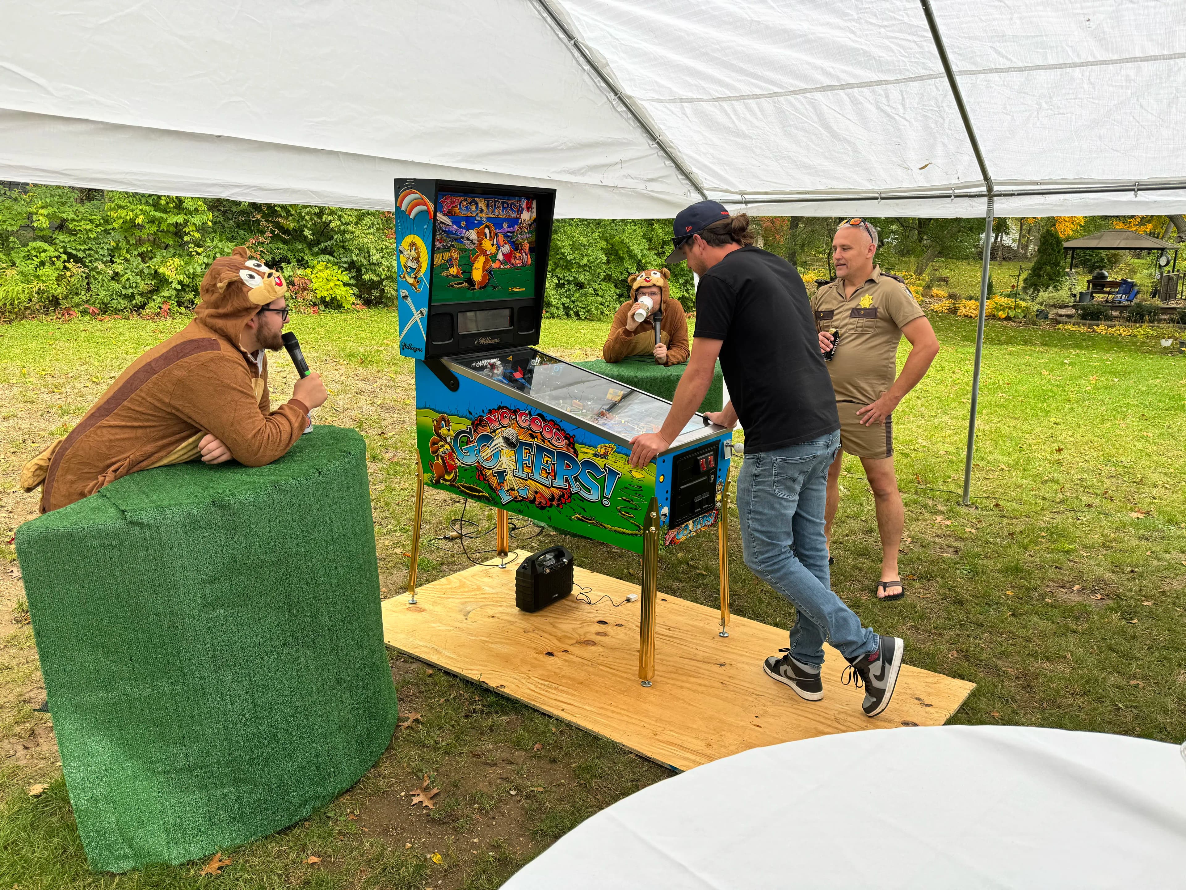 People in costumes playing Gophers pinball machine under a white tent