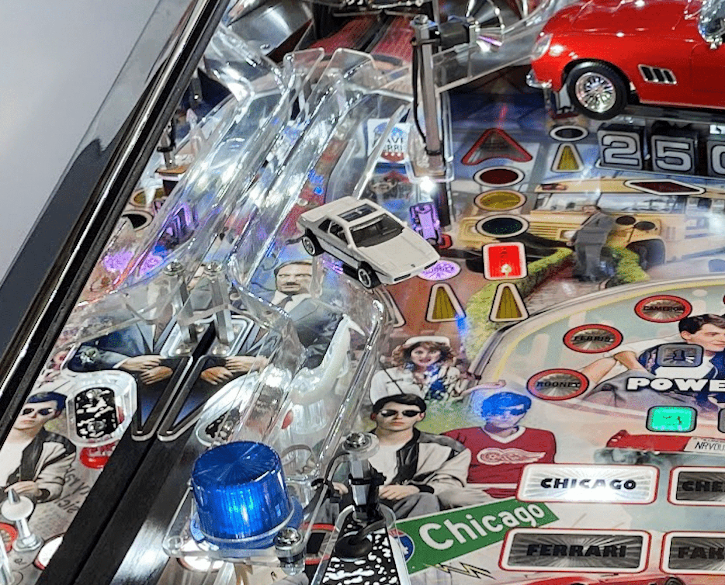 Detailed pinball machine playfield with cars, lights, and stylized characters