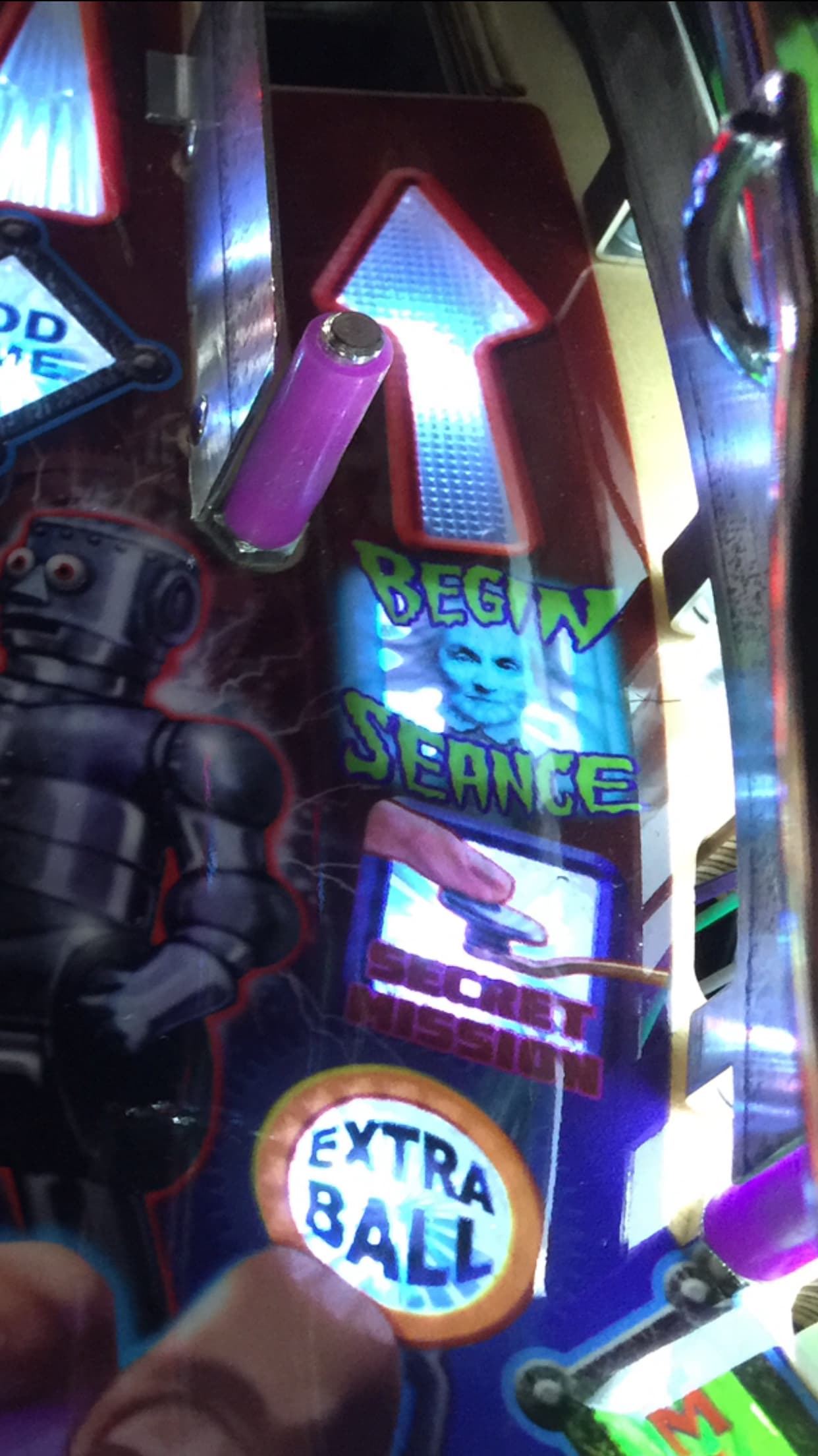 Pinball machine close-up with neon colors, robot, and "Begin Seance" text