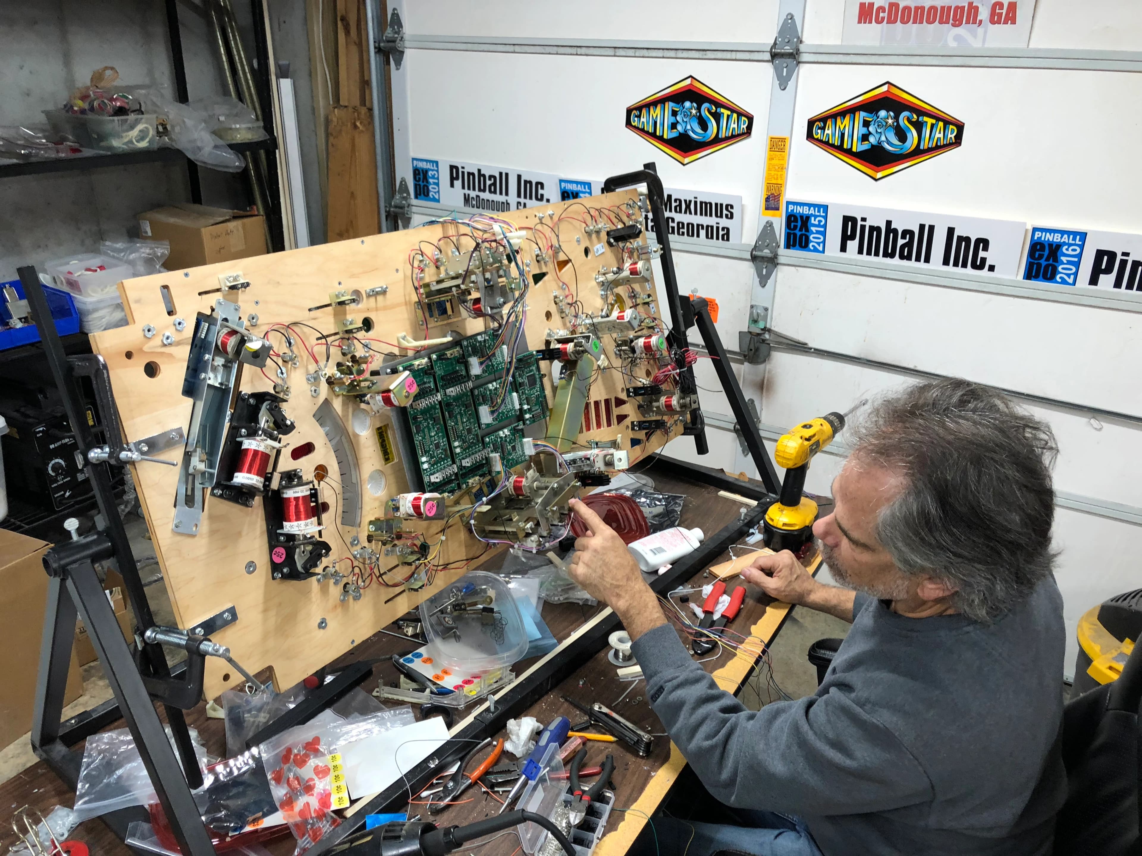 Technician repairing pinball machine circuit board at Pinball Inc workshop