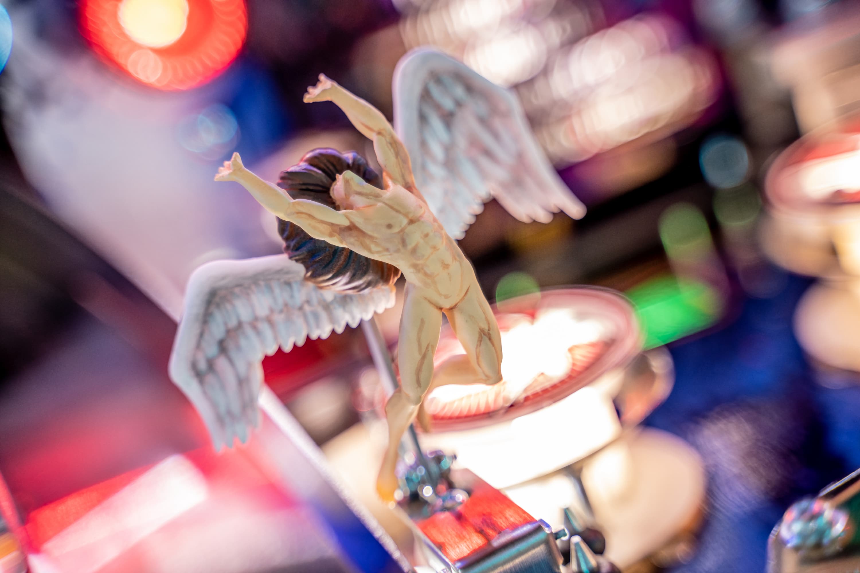 Winged figurine with outstretched arms on colorful blurred background