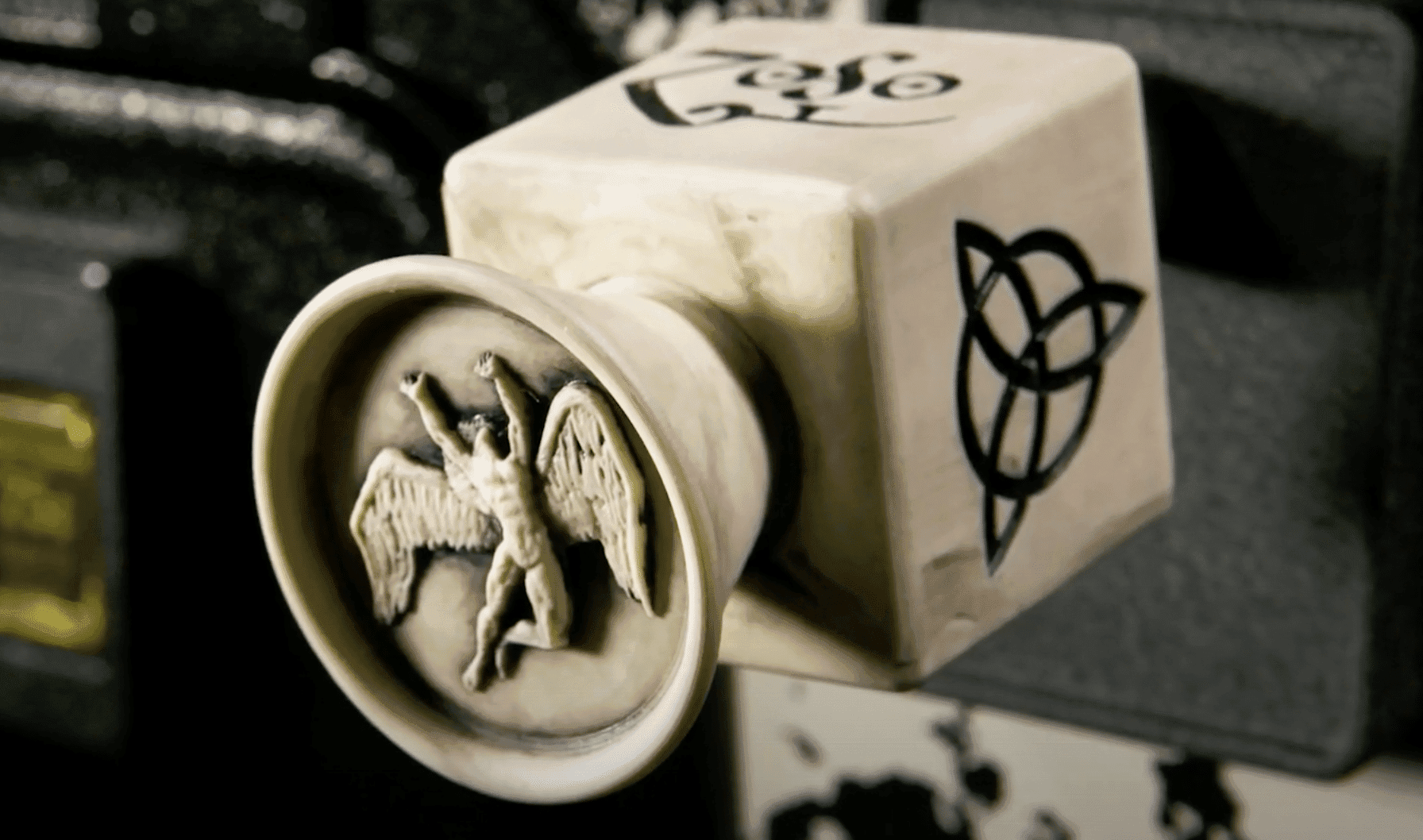 Decorative ceramic cube with winged figure emblem and geometric symbol