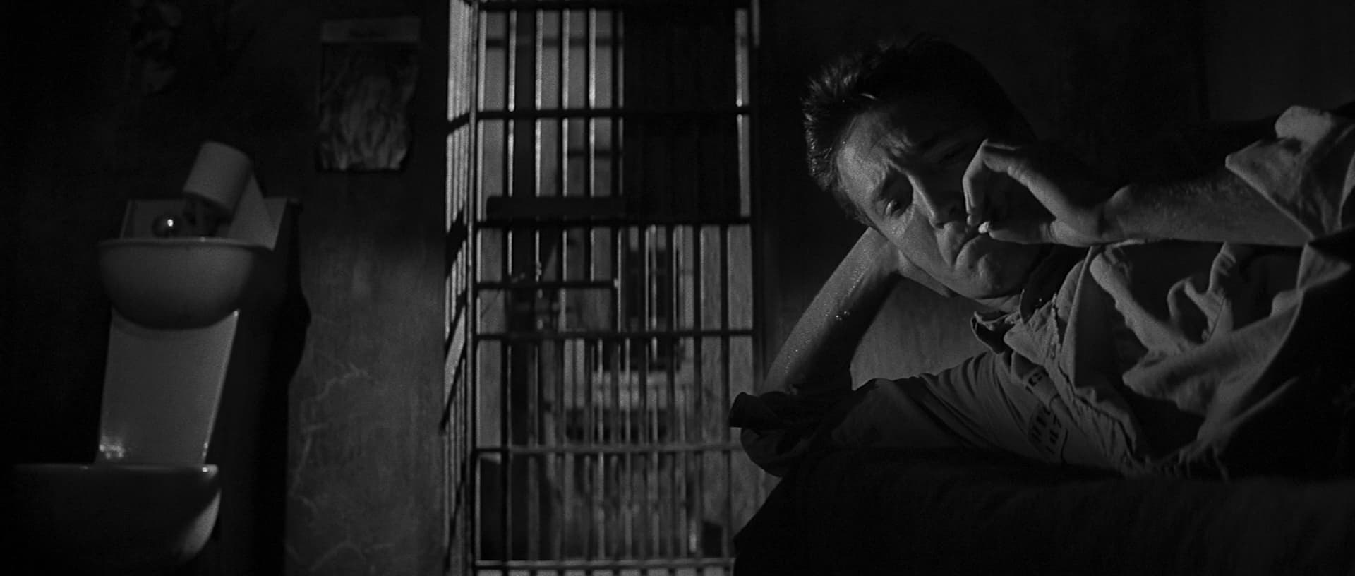 Black and white scene of someone behind jail bars looking distressed