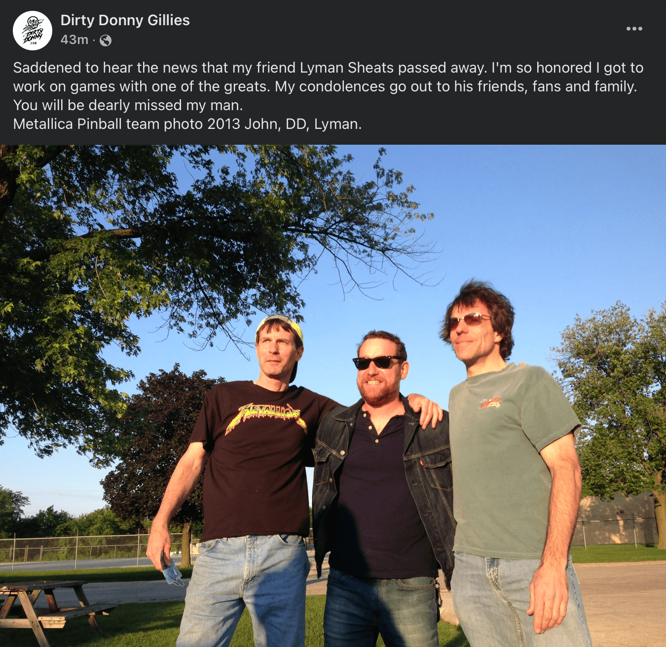 Three friends in Metallica shirts pose together outdoors near trees