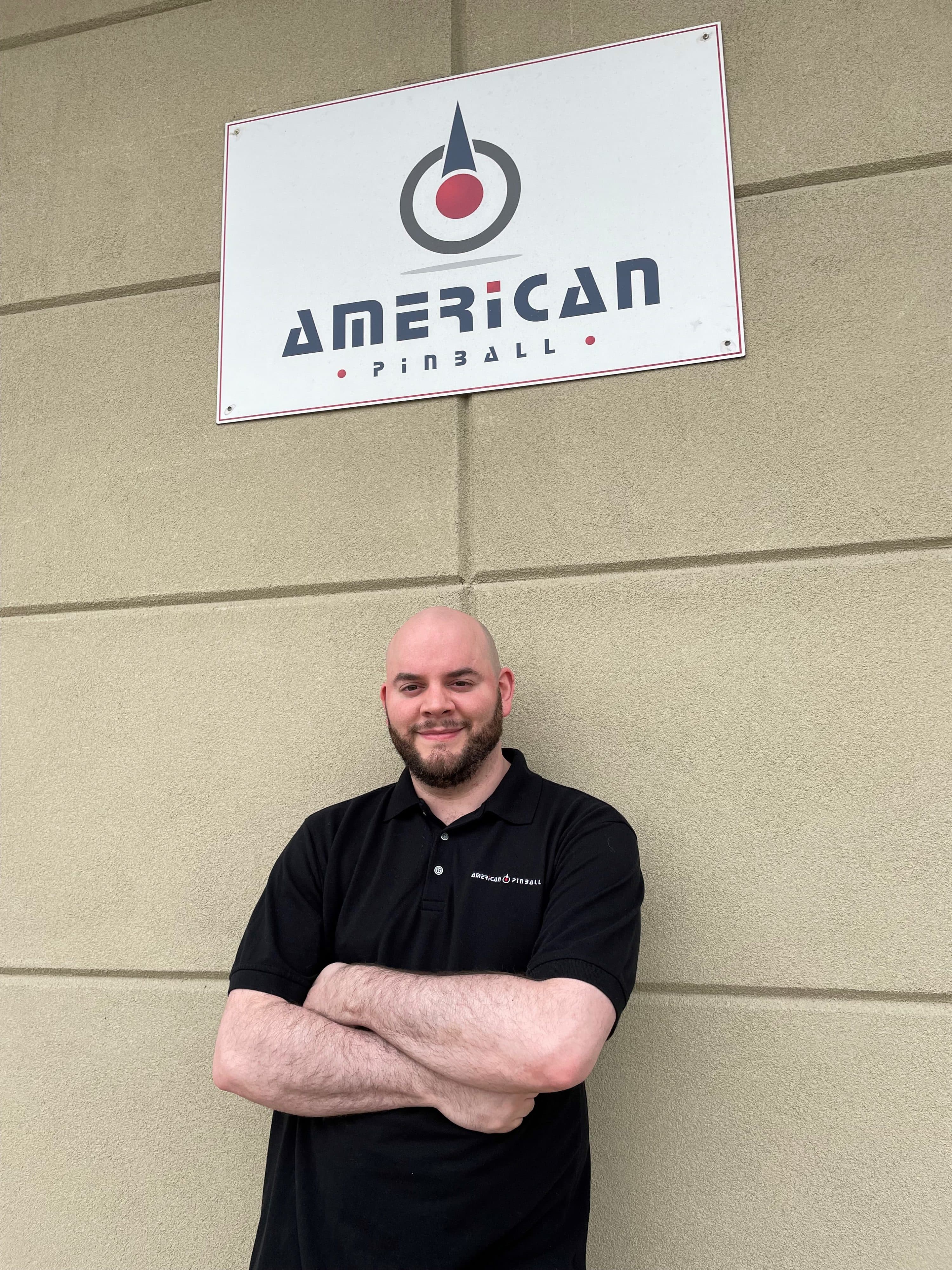 Employee standing under American Pinball logo with crossed arms