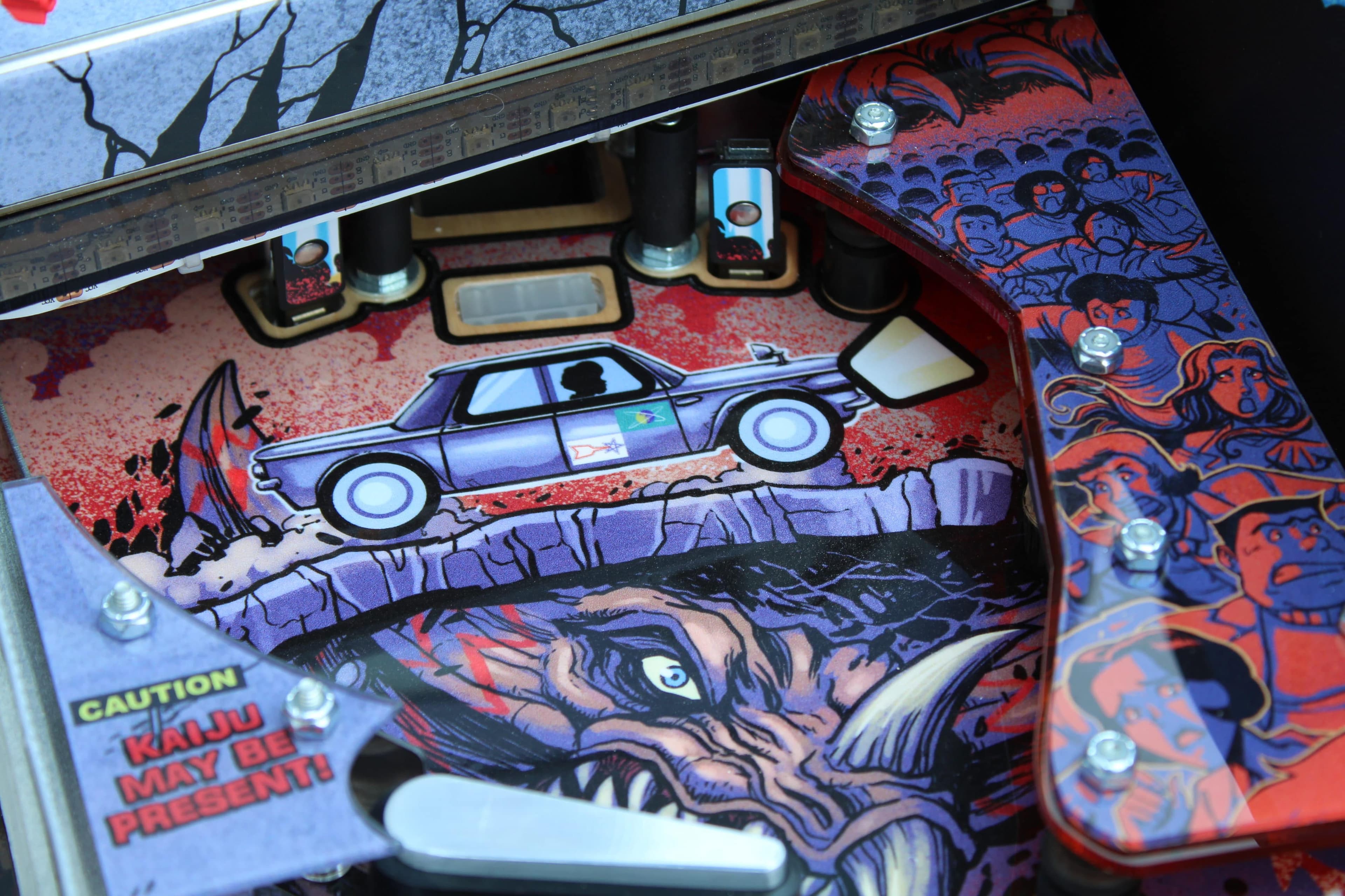 Colorful pinball machine with car, dragon, and "Kaiju May Be Present" warning
