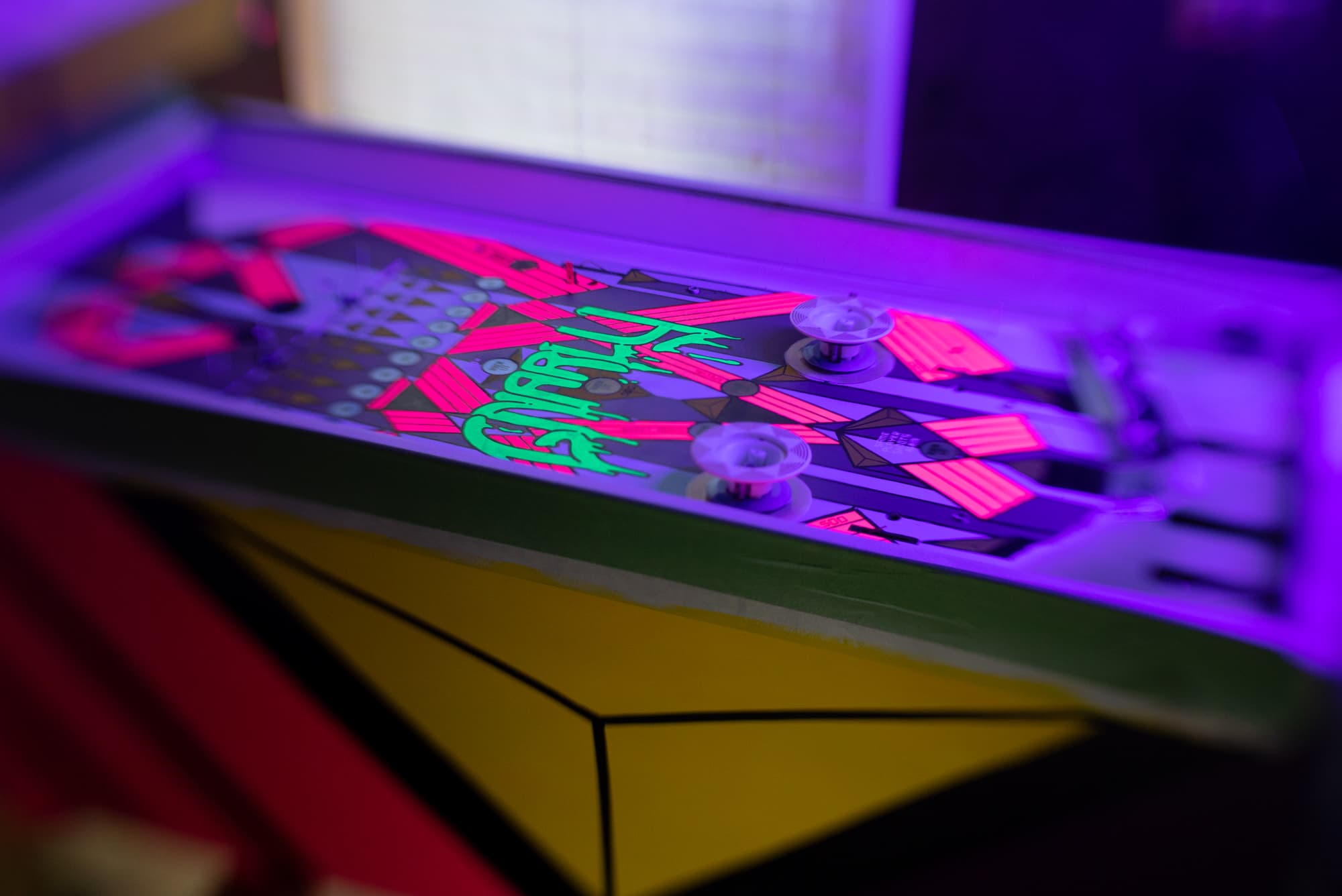 Skateboard with vibrant neon pink and green graphic design under purple light