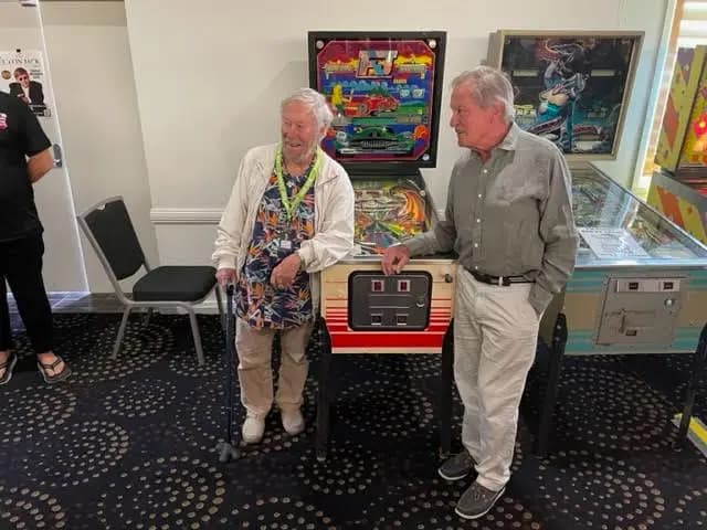 Two older men standing near colorful pinball machines in a museum exhibit