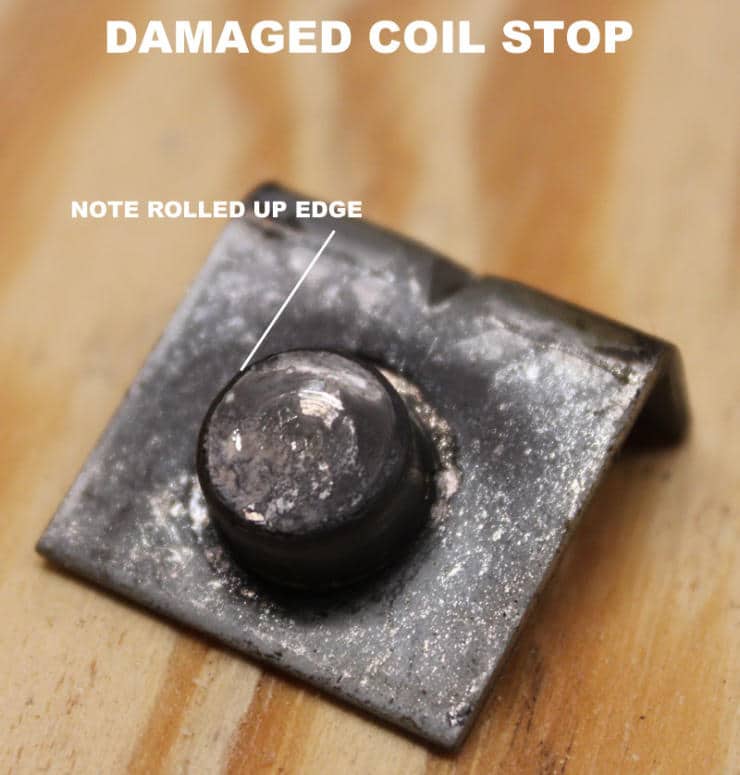 Damaged metal coil stop with rolled-up edge on wooden surface